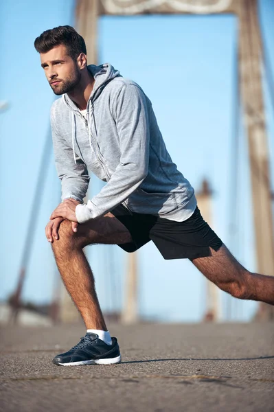 Man stretching his body before running while standing on the bridge — Stock Photo, Image