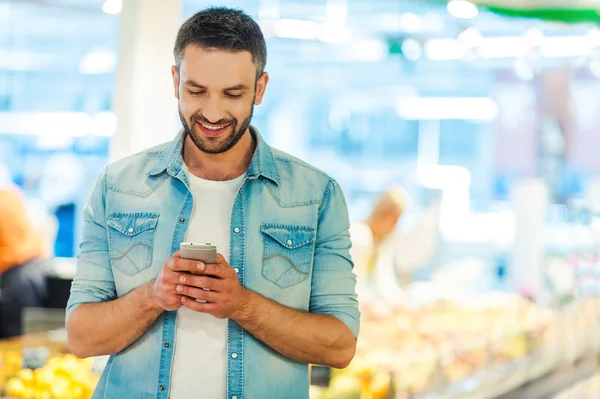 Hombre sosteniendo el teléfono móvil en la tienda de alimentos —  Fotos de Stock