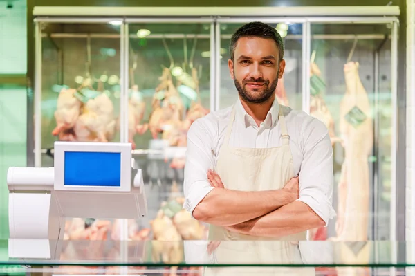 Butcher standing at supermarket checkout with meat — Stockfoto