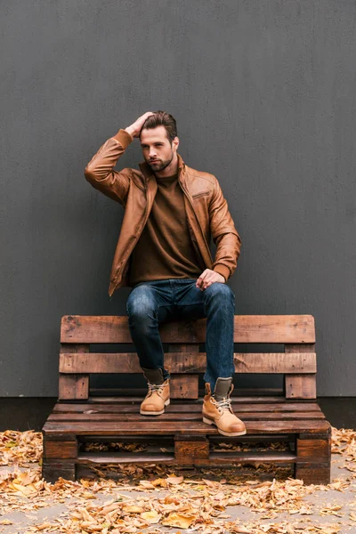 Przystojny mężczyzna siedzi na drewnianych paletach — Zdjęcie stockowe