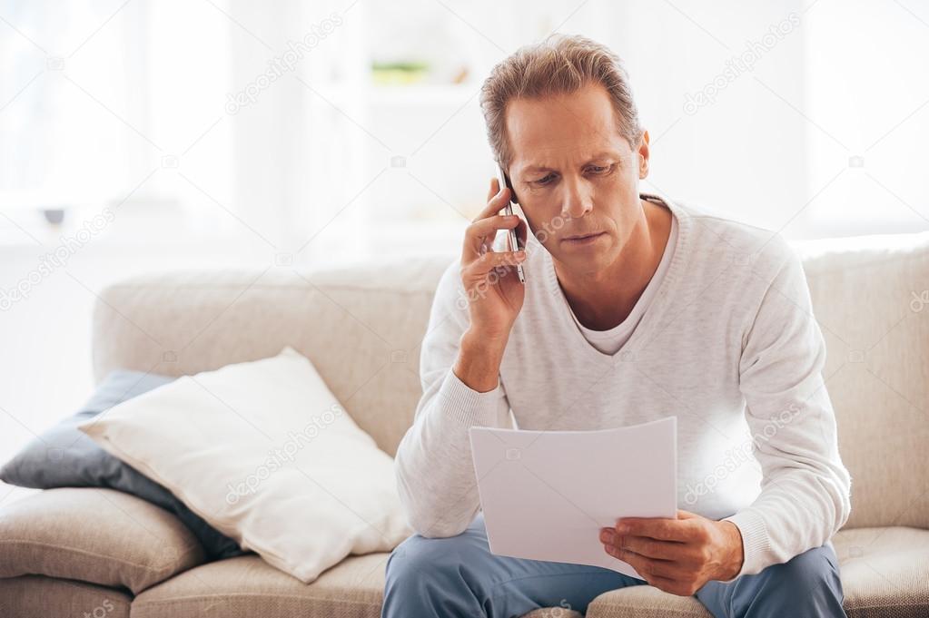 mature man holding paper and talking on phone