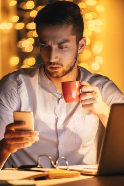 Uomo guardando smart phone e tenendo in mano tazza — Foto Stock