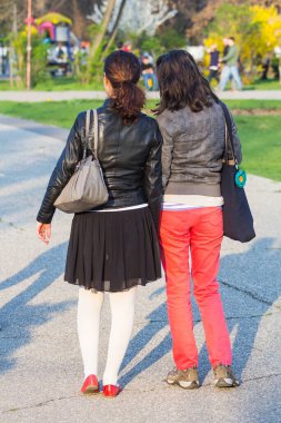 Ayakta duran, ileriye bakan ve el ele tutuşan iki kadının arka fotoğrafı. 