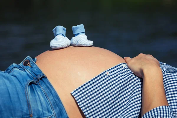 妊娠中の母親の腹に赤ちゃんのための靴下のペアの閉鎖 — ストック写真