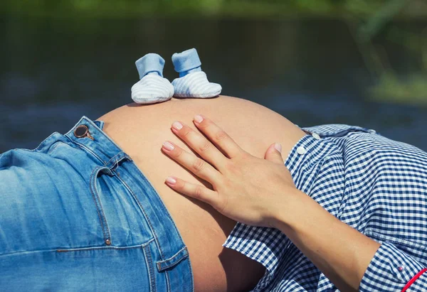 赤ちゃんの靴下のペアを持っている間 彼女の妊娠中の腹に触れる母親の手の閉鎖 — ストック写真