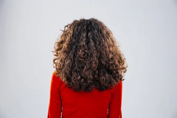 Back pose of a woman with beautiful curly in a red blouse posing at studio