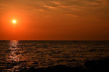 Arnavutluk 'un Saranda kenti yakınlarında, denizin üzerinde kızıl gün batımı, kara bulutlar ve ışık ışınlarıyla dolu.