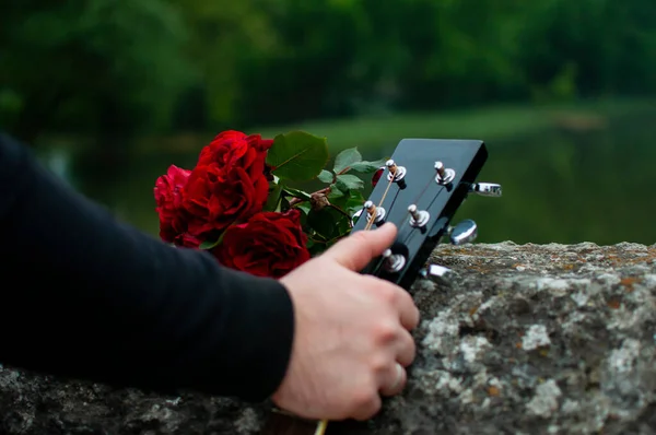 Man's hand tightly holding guitar and bouquet of roses next to guitar at the fence of the Roman Bridge in Sarajevo