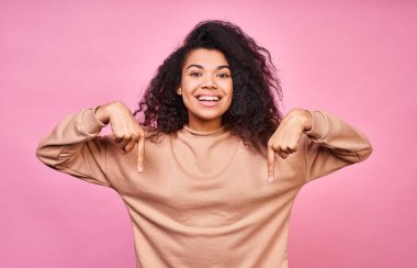 Güzel, sağlıklı tenli esmer bir kadın, mutlu görünüyor, sanki aşağıya bakıyor gibi, düz görünüyor ve gülümsüyor, pembe arka planda soyutlanmış. Güzel bir genç kadın aşağıda inanılmaz bir şey görür..