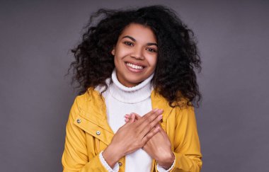 Mutlu siyahi bir kadının kapalı çekimleri yemin eder ya da söz verir, elini göğsüne koyar, doğruyu söyler, kameraya dostça bakar, büyüleyici bir gülümsemesi vardır, beyaz bir süveter giyer ve sarı bir ceket giyer..