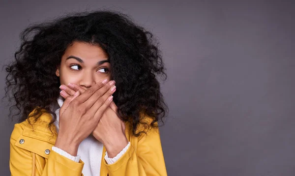 神秘的で遊び心のあるかわいいアフリカ系アメリカ人の若い女性が彼女の手で彼女の口をカバーし 秘密を停止しようとして 側面に見える巻き毛と黄色のジャケットを持っています スペースのコピー — ストック写真