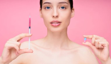 Çekici, kahverengi saçlı, çıplak omuzlu bir kadın elinde güzellik iğnesi ve elinde bir hapla bir seçim yapıyor. Gençlik ve enjeksiyon cerrahisi.