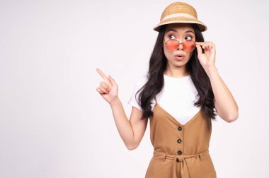 Koyu renk uzun saçlı, çekici görünümlü, sıradan beyaz tişört ve kırmızı gözlüklü bir Asyalı kadın beyaz bir arkaplana karşı duran boş bir fotokopi alanını işaret ediyor. Şuraya bak..