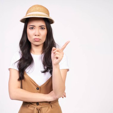 Düşünceli, huysuz, mutsuz, koyu renk uzun saçlı, saman şapkalı, stüdyoda beyaz bir arkaplanda poz veren üzgün bir Asyalı kadın. Boşluğu kopyala.