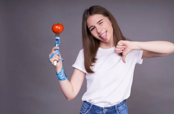 陽気なスキニー可愛いですCaucasian女の子でAホワイトTシャツ保持していますトマト上のフォークで測定テープとともに嫌悪感の兆候 食事中の女の子 カロリーを数える — ストック写真