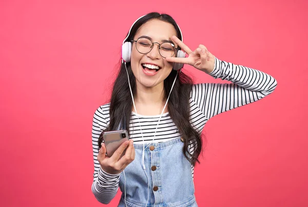 充满热情的亚洲女孩 头戴白色耳机 穿着整齐的毛衣 听着音乐 玩得很开心 感觉充满活力 被粉色背景隔离 复制空间 — 图库照片