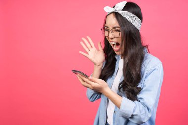 Kızgın ve üzgün genç Asyalı kadın, kot ceketli ve yuvarlak gözlüklü, hayal kırıklığına uğramış duygularıyla telefonda bağırıyor. Pembe arka planda izole edilmiş. Boşluğu kopyala.