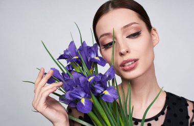 Yakın plan, genç, alımlı bir kız, akşam makyajı ile, güzel bir moda akşamı, siyah bir elbise, bir buket bahar mavi süsen tutar ve aşağı bakar.