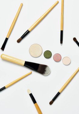 Dikey çekim, rastgele yerleştirilmiş profesyonel makyaj fırçaları, simetrik olarak çıplak göz farı paleti, beyaz arka planda izole edilmiş. Üst Manzara, düz çizgi. Makyaj konsepti, kozmetik, imaj.