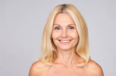 Güzel, 50 'li yaşlarda olgun bir kadın beyaza izole edilmiş kameraya bakıyor. Olgun, yaşlı bir kadın portresi. Sağlıklı yüz bakımı güzellik, orta yaşlı cilt estetiği, kozmetoloji konsepti.