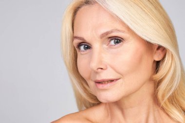 Çekici, güzel, çekici bir kadının yakın plan portresi krem, merhem, maske, losyon, gri arka planda izole edilmiş mükemmel cilde sahip. Kadın olgun güzellik kavramı, yetişkin teni. Boşluğu kopyala.