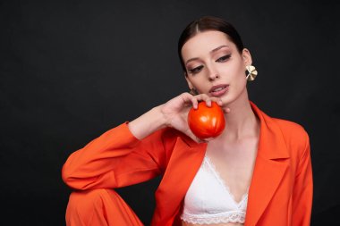 Stüdyoda siyah arka planda turuncu bir takım elbise giymiş çekici bir kadın model..