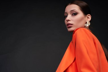 Alt açı, gece makyajlı çekici ve şık bir kadının portresi stüdyoda koyu bir arkaplan karşısında turuncu bir takım elbiseyle poz veriyor. Boşluğu kopyala.