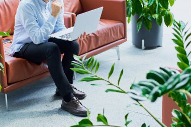 Gömlekli bir gencin elinde dizüstü bilgisayarla modern bir ofisin penceresinin yanındaki masada otururken yan görüntüsü. İş konsepti, serbest çalışma. Yüzü olmayan.