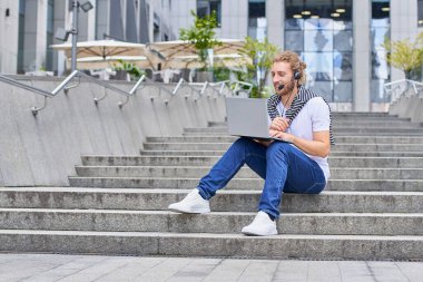 Modern parkın dışında bilgisayarla çalışan yakışıklı bir genç. Uzaktan kumandalı bir işte çalışıyor. Yaz tarzında. Kentsel yaşam tarzı insanları.