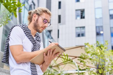 Boş zaman, eğitim ve insan konsepti. Şehirdeki çizim ve çizimler için defteri, günlüğü ya da eskizi olan genç bir moda adamı notlar alır, çizimler yapar..