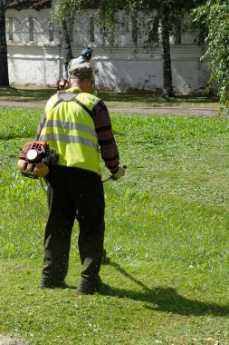 Yazın çim biçme makinesiyle çimleri biçen bir adam.