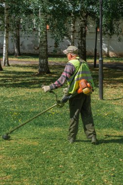 Yazın çim biçme makinesiyle çimleri biçen bir adam.