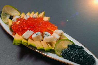 Kırmızı ve siyah havyarlı avokado dilimleri ve renkli bir tabakta küflü peynir.