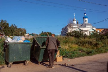 Evsiz bir adam tapınağın arka planında çöp kutusunu karıştırıyor.