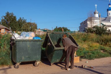Evsiz bir adam tapınağın arka planında çöp kutusunu karıştırıyor.