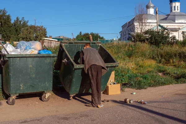 一个无家可归的人在寺庙的背景下在垃圾筒里翻找 — 图库照片