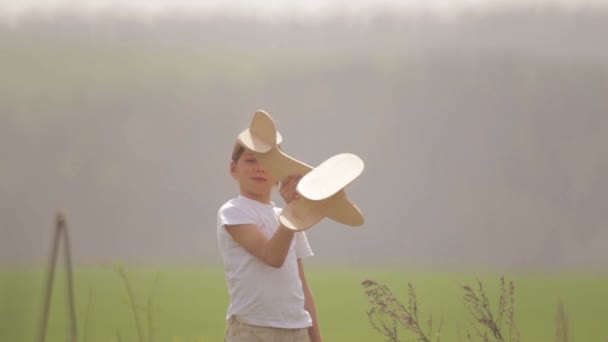 Caucasian boy playing with a model airplane. Portrait of a child with a wooden plane in a field. Boy in nature plays with the layout of the aircraft. — Stock Video