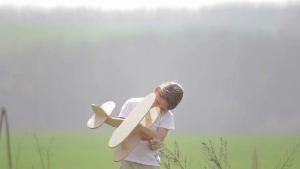 Kaukasische jongen spelen met een modelvliegtuig. Portret van een kind met een houten vliegtuig in een veld. Jongen in de natuur speelt met de indeling van het vliegtuig. — Stockvideo