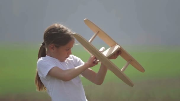 Kaukasischer Junge beim Spielen mit einem Modellflugzeug. Porträt eines Kindes mit einem Holzflugzeug auf einem Feld. Junge in der Natur spielt mit dem Layout des Flugzeugs. — Stockvideo
