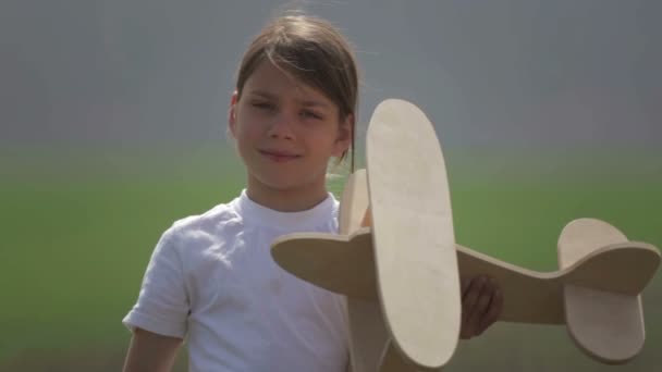 Kaukasische jongen spelen met een modelvliegtuig. Portret van een kind met een houten vliegtuig in een veld. Jongen in de natuur speelt met de indeling van het vliegtuig. — Stockvideo