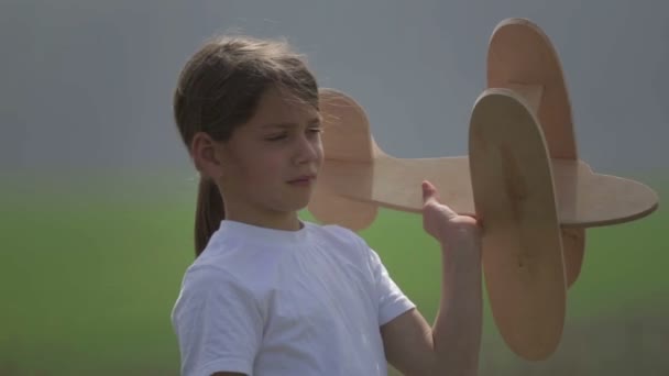 Rapaz caucasiano a brincar com um avião modelo. Retrato de uma criança com um avião de madeira em um campo. Menino na natureza brinca com o layout da aeronave . — Vídeo de Stock