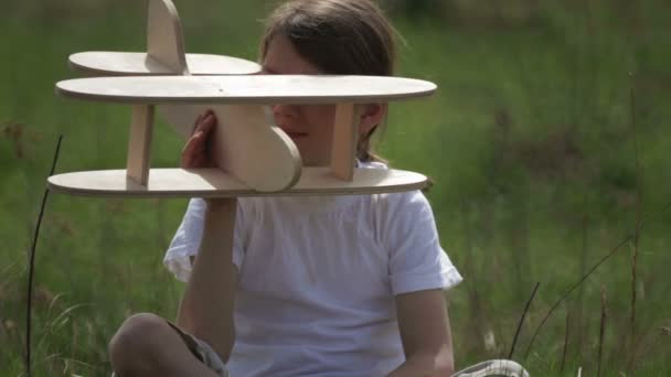 Kaukasische jongen spelen met een modelvliegtuig. Portret van een kind met een houten vliegtuig in een veld. Jongen in de natuur speelt met de indeling van het vliegtuig. — Stockvideo