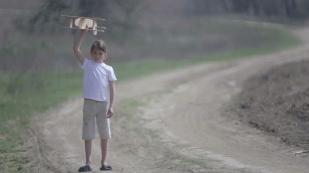 Ragazzo caucasico che gioca con un aeroplano modello. Ritratto di un bambino con un piano di legno in un campo. Ragazzo in natura gioca con il layout del velivolo . — Video Stock