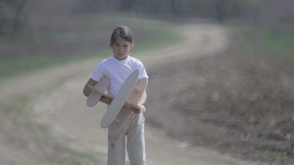 Caucasian boy playing with a model airplane. Portrait of a child with a wooden plane in a field. Boy in nature plays with the layout of the aircraft. — Stock Video