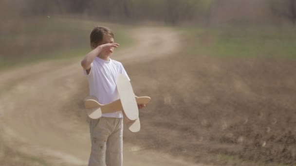 Chico caucásico jugando con un avión modelo. Retrato de un niño con un plano de madera en un campo. Niño en la naturaleza juega con el diseño de la aeronave . — Vídeos de Stock