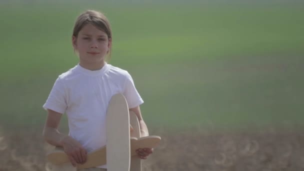 Kaukasische jongen spelen met een modelvliegtuig. Portret van een kind met een houten vliegtuig in een veld. Jongen in de natuur speelt met de indeling van het vliegtuig. — Stockvideo