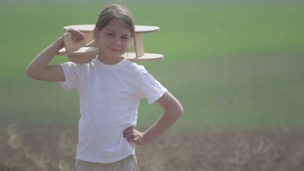 Chico caucásico jugando con un avión modelo. Retrato de un niño con un plano de madera en un campo. Niño en la naturaleza juega con el diseño de la aeronave . — Vídeos de Stock