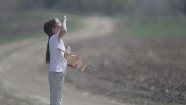 Chico caucásico jugando con un avión modelo. Retrato de un niño con un plano de madera en un campo. Niño en la naturaleza juega con el diseño de la aeronave . — Vídeos de Stock