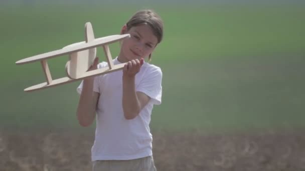 Ragazzo caucasico che gioca con un aeroplano modello. Ritratto di un bambino con un piano di legno in un campo. Ragazzo in natura gioca con il layout del velivolo . — Video Stock