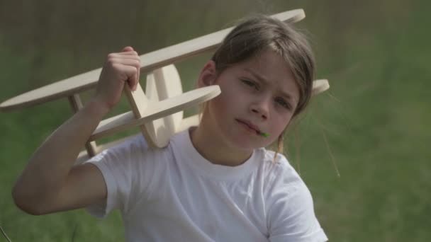 Caucasian boy playing with a model airplane. Portrait of a child with a wooden plane in a field. — Stock Video
